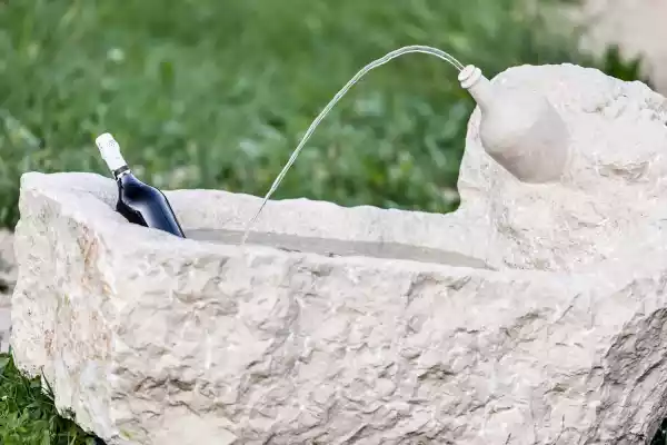 Gartenbrunnen mit Prosecco-Flasche als Wasserauslauf realisiert aus einem Kalksteinfindling von Jacob Steinmetz Neumarkt in Südtirol