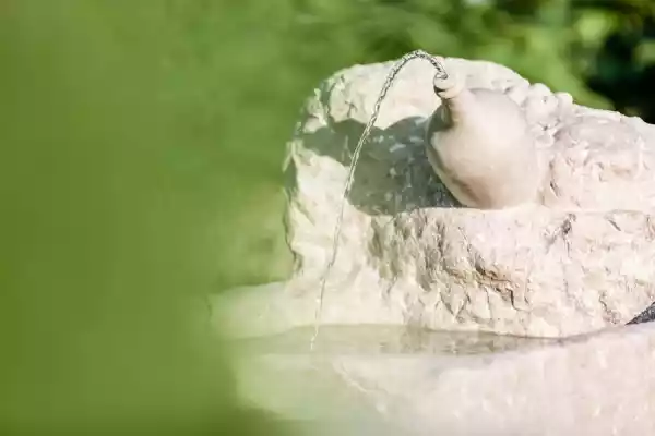 Prosecco-Flasche als Steinskulptur auf einem Brunnen aus Naturstein