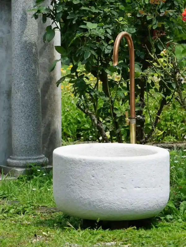 Runder Brunnen aus hellem Kalkstein mit Wasserhahn aus Kupfer und Messing