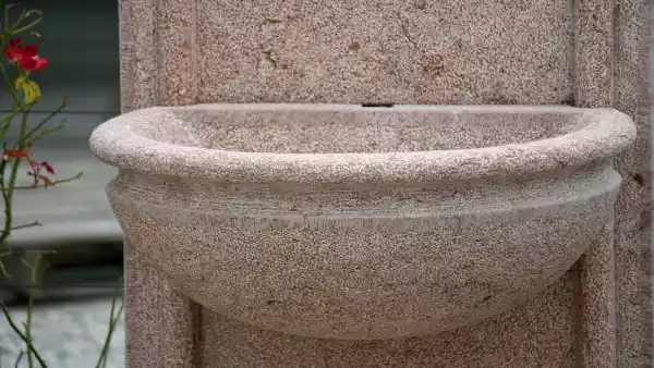 La superficie della fontana a muro in pietra naturale è stata finemente bocciardata - così è facile da pulire
